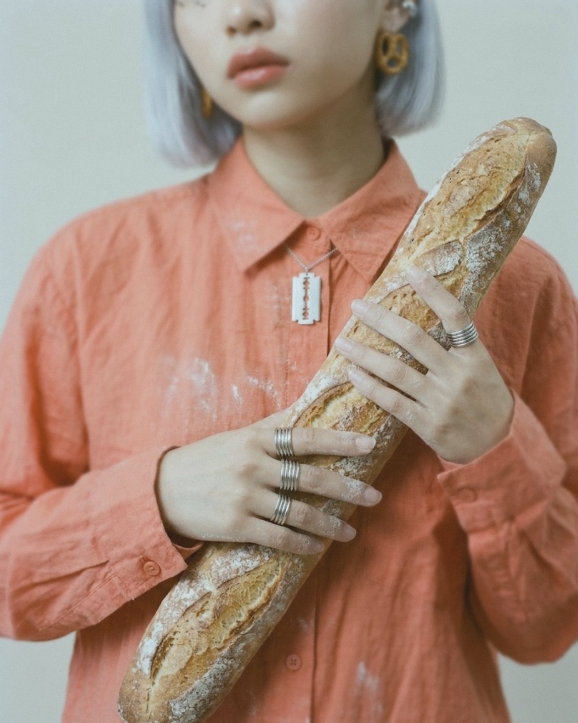 A long baguette held across a floury coral shirt.