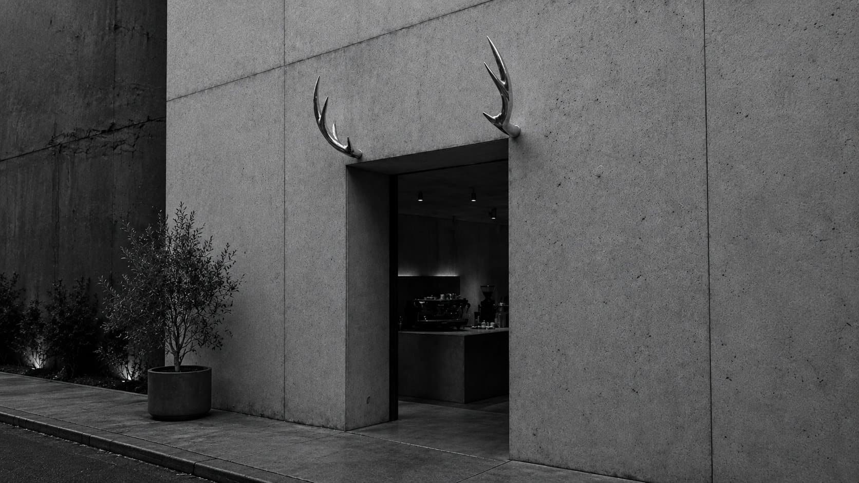 The café entrance in concrete, two metal antlers mounted above the door