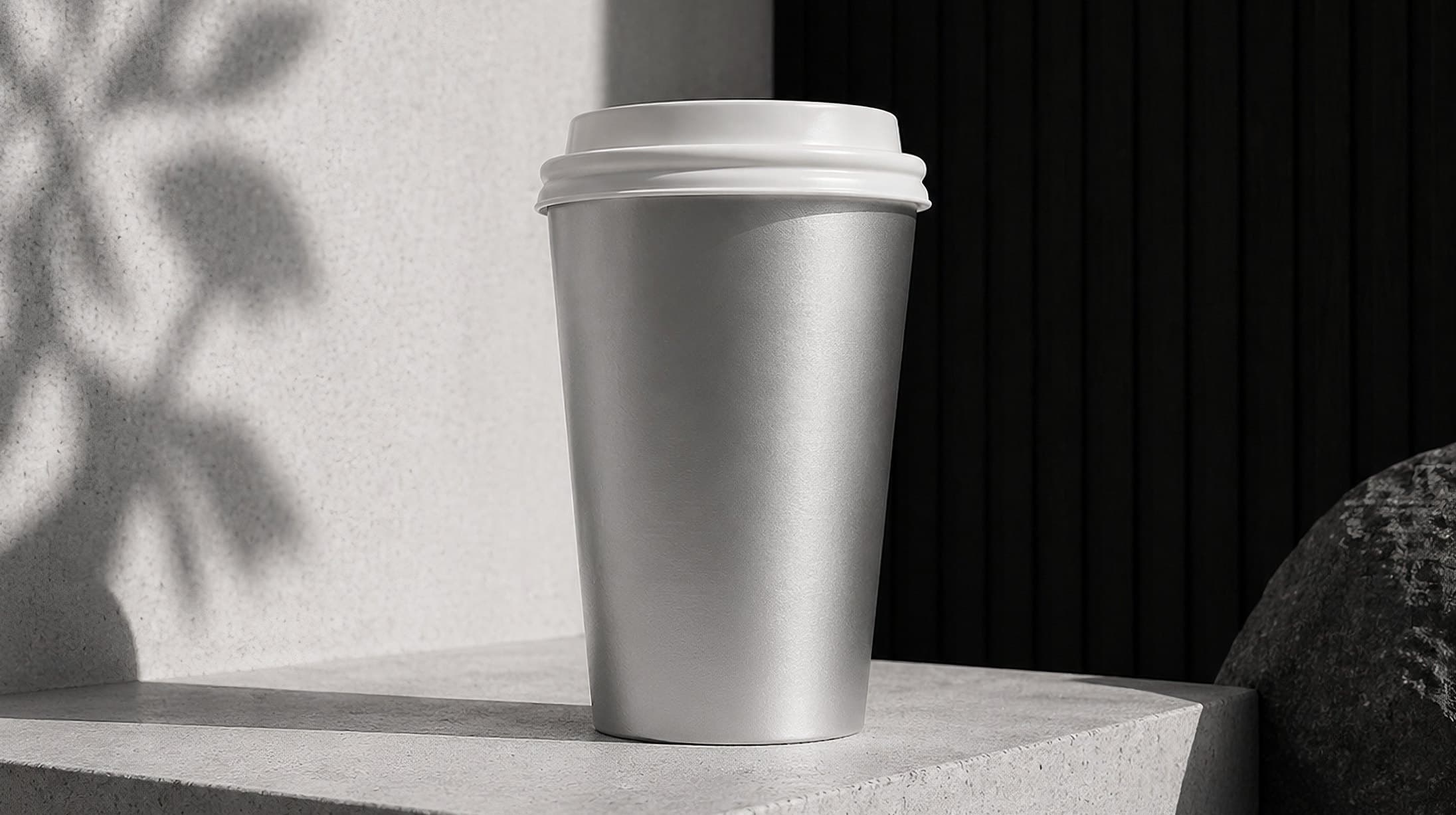 An aluminium takeaway cup on a stone ledge, leaf shadows on the wall