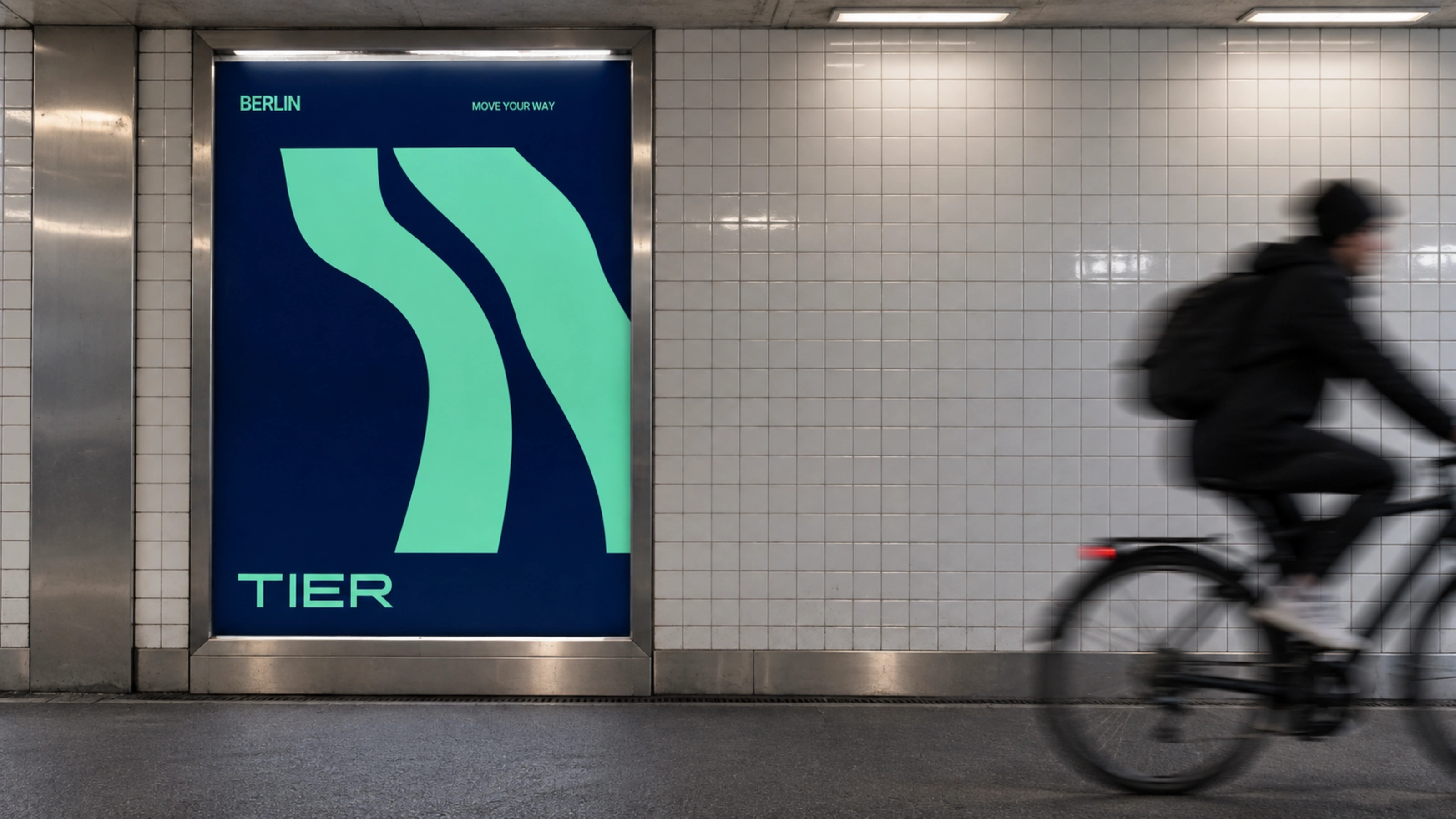 A TIER poster with two ribbons in a Berlin underground station, a cyclist passing.