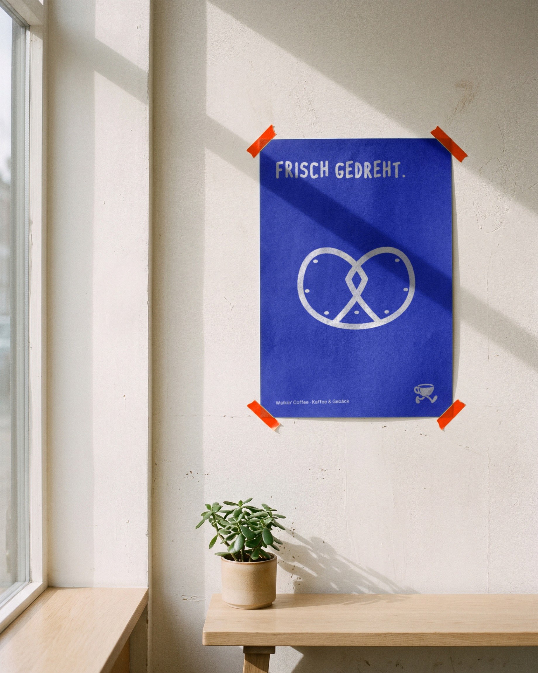Ein blaues Plakat mit einer gezeichneten Brezel, an die Wand des Cafés geklebt.