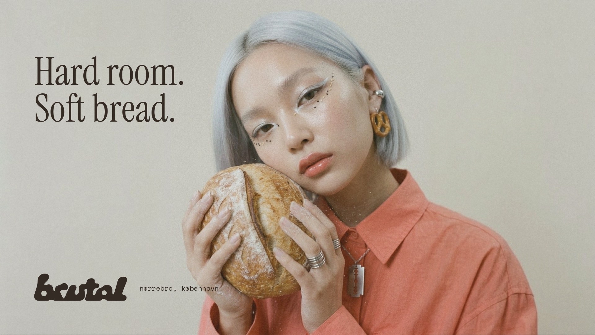 A baker holding a round sourdough loaf against her cheek, with the line Hard room. Soft bread.